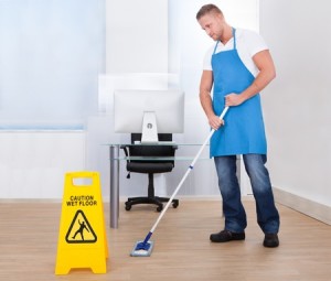 27393718 - yellow warning notice to caution people to a slippery wet surface as a janitor mops the floor in an office building